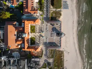 Bird's eye view of a building on a beach with a walkway surrounded by plants and trees.