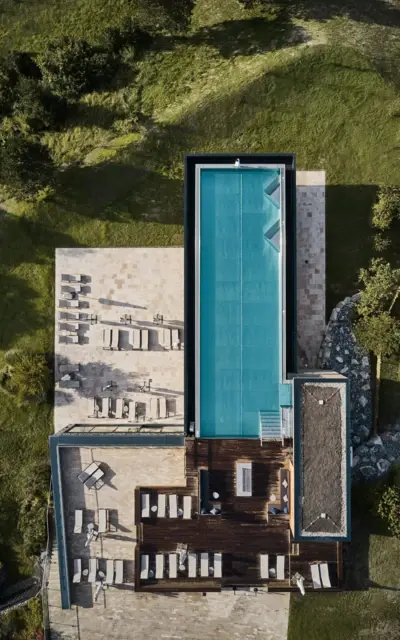 Pool with sun loungers on the roof terrace of a building, surrounded by grass and plants, taken from a bird's eye view.