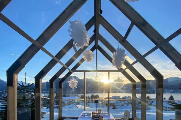 Tegernsee in winter A table with chairs under a glass canopy, with snow and mountains in the background.