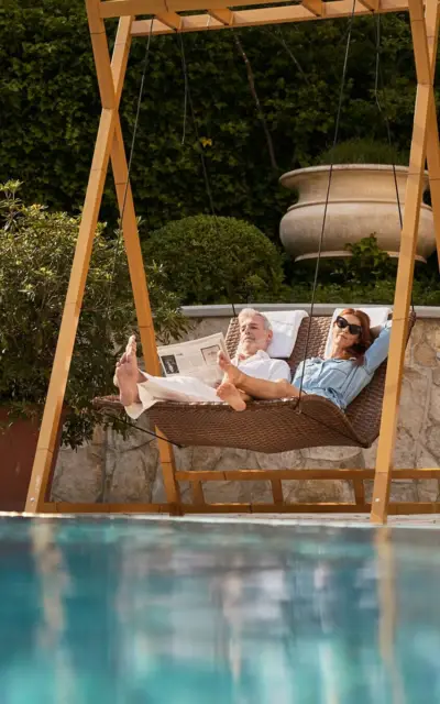 Man and woman lying in a hanging swing at the edge of the pool.