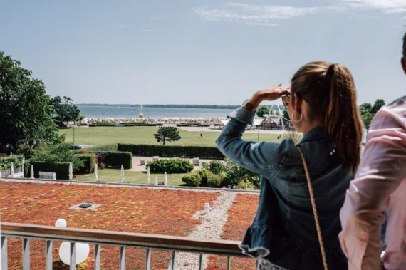 A woman standing on a balcony looking onto the beach and sea. 