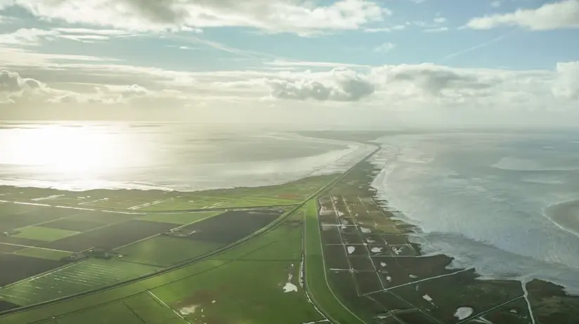Aerial view of the island of Sylt with adjacent water, surrounded by clouds and a cloudy sky.