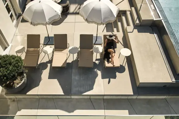 A woman sitting on a deck chair under an umbrella outdoors.