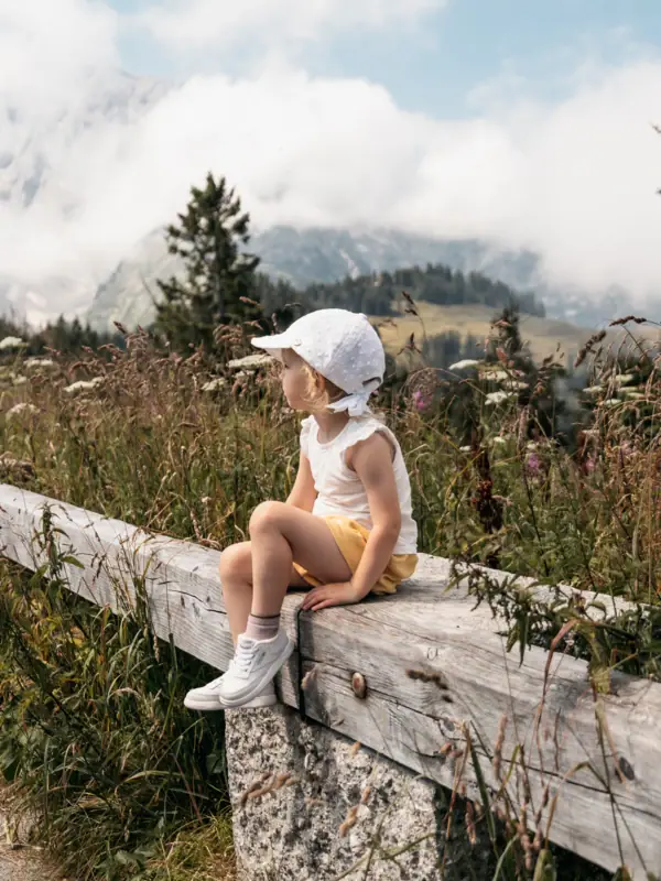 A girl is sitting on a fence outdoors.