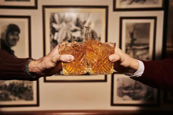 Two hands holding glasses with liquid splashing.