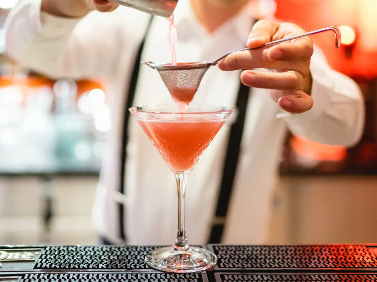 Bar A-ROSA Travemünde Ein Barkeeper gießt ein rotes Getränk in ein Martiniglas.
