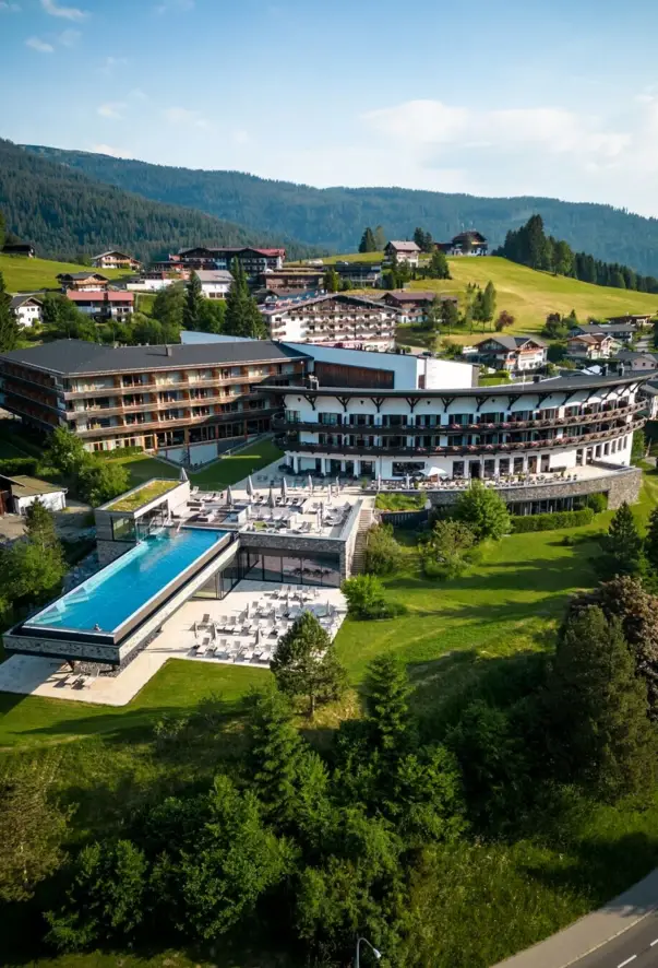 A building with an infinity pool in the middle of a mountain village, surrounded by trees and green spaces.