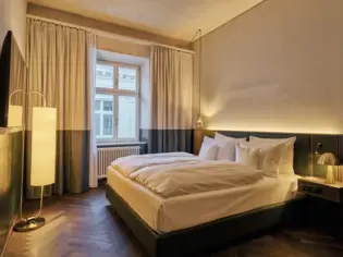 A hotel room with a large bed with white bed linen and a window in the background.