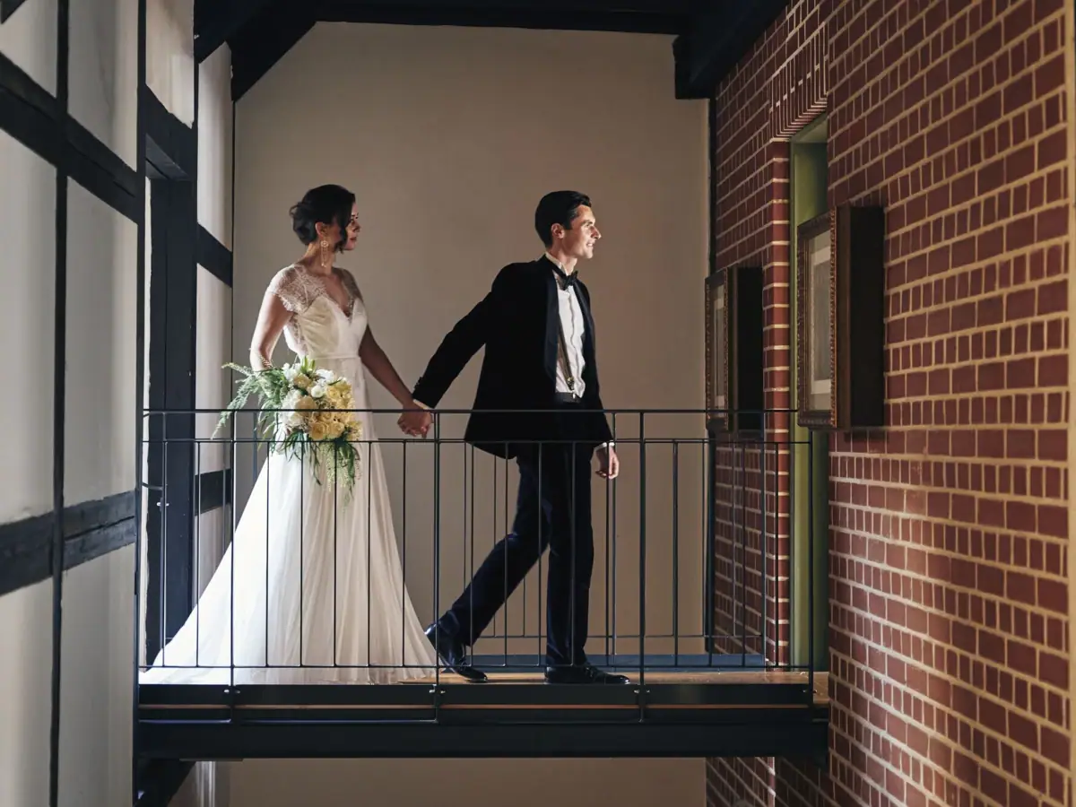 Ein Mann und eine Frau in Hochzeitskleidung halten Händchen und gehen über einen Gang.