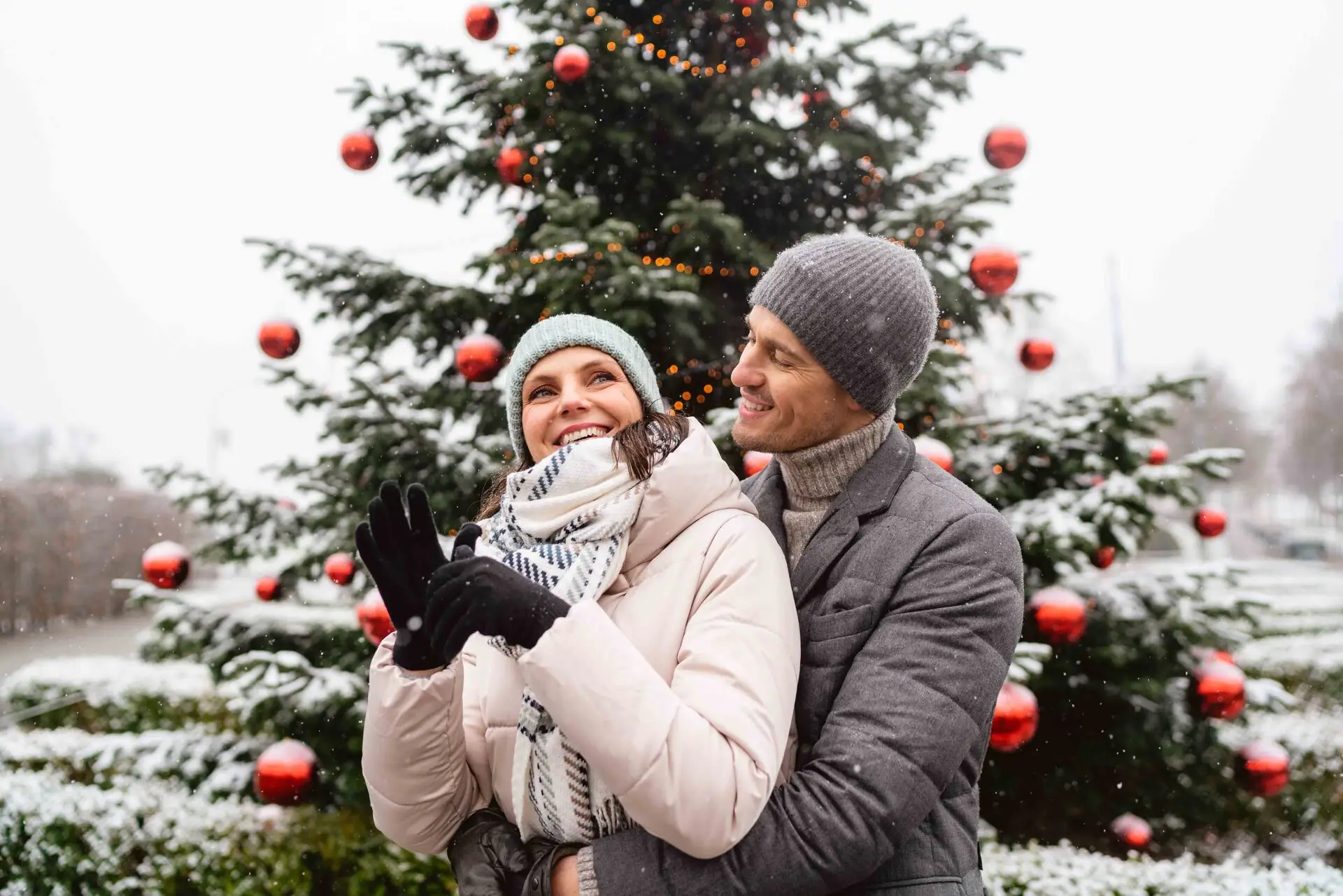A man and a woman are standing in front of a Christmas tree.