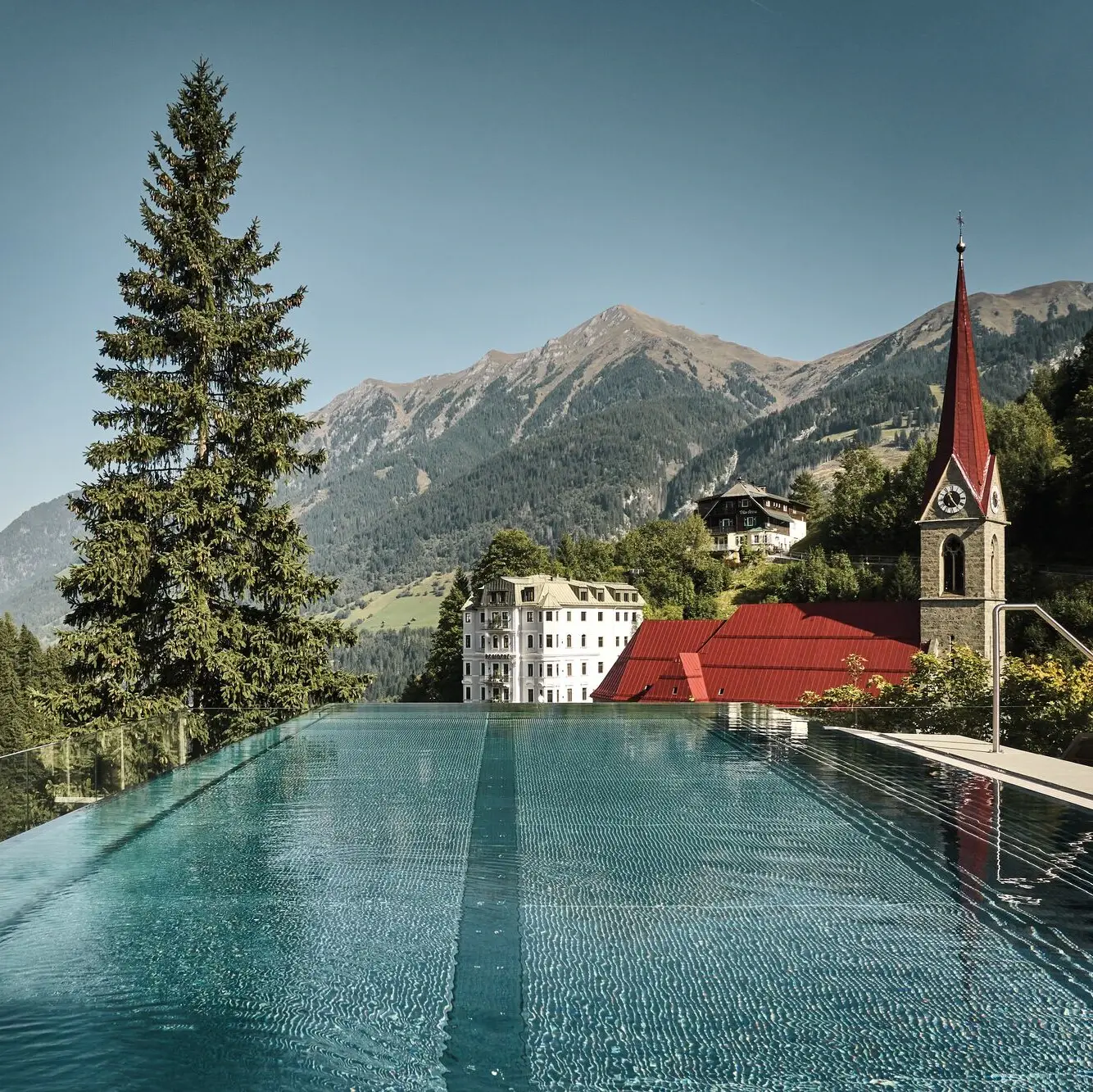 Rooftop infinity pool at the Straubinger Grand Hotel in Bad Gastein with panoramic mountain views and historic church.