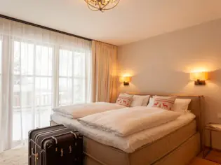 A beige upholstered bed stands against a white wall with white bed linen and two Christmas decorative cushions with reindeer on them.