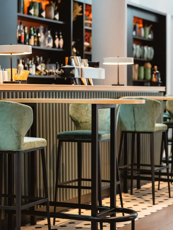 Eine Bar mit grünen Stühlen und einem schwarzen Regal mit Flaschen.