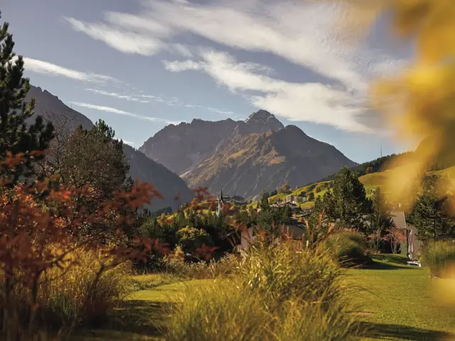 Autumn landscape with a mountain in the background, surrounded by grass, trees and clouds.