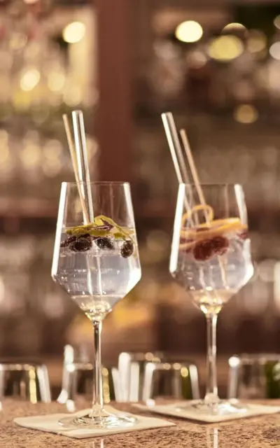 Two wine glasses filled with a gin creation and glass straws on a counter.