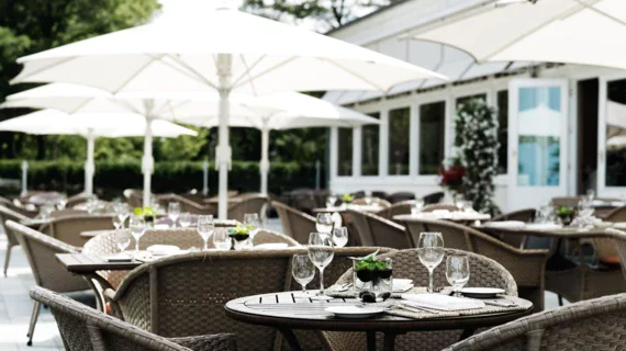 An outdoor dining setup with a table and chairs under an umbrella, featuring a tablecloth.