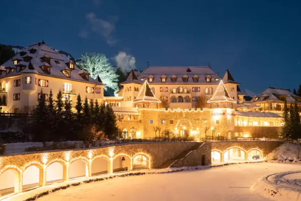 The snow-covered A-ROSA Kitzbühel is warmly illuminated in the dark and the surrounding landscape is covered in snow.