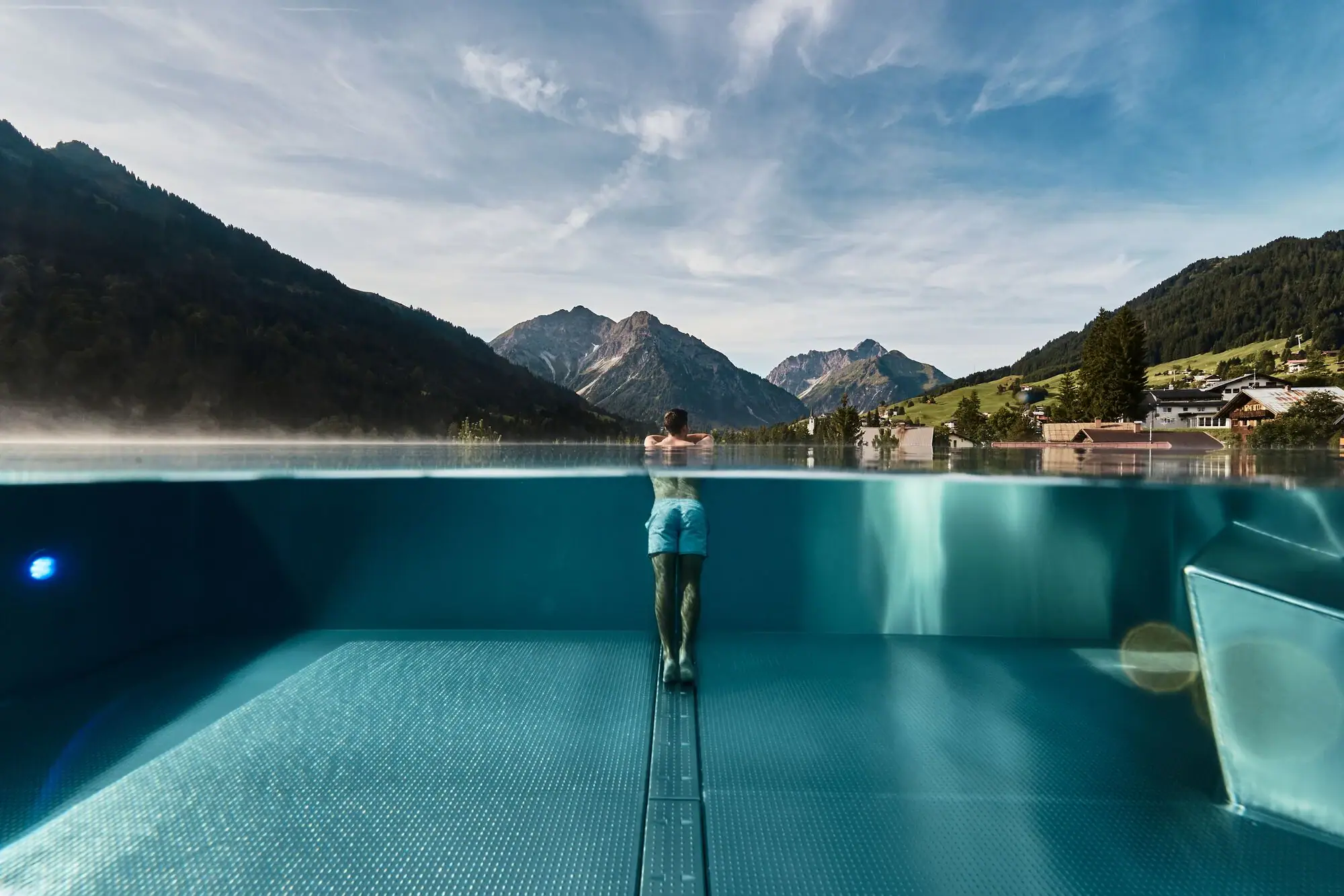 A person stands in a pool with mountains in the background.