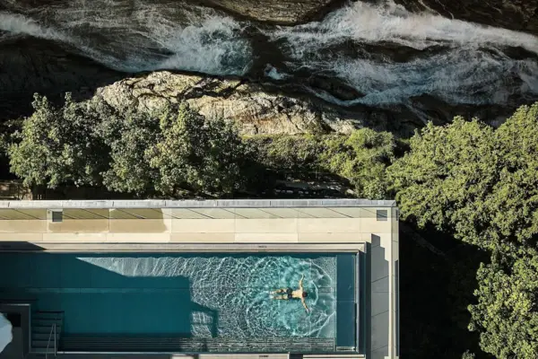 A long outdoor pool was photographed from above from a bird's eye view, in which a man is swimming. A waterfall can also be seen in the upper part of the picture.