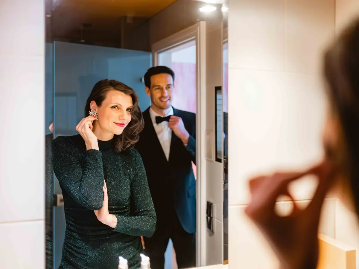 NYE A man in a suit putting on earrings indoors.