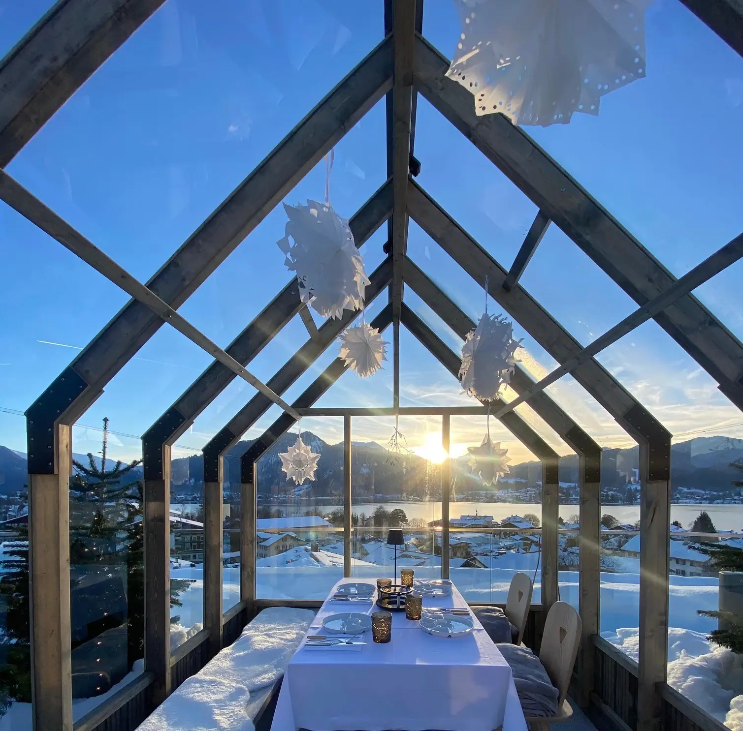 A table with chairs under a glass roof, with snow and mountains in the background.
