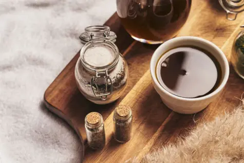 A cup of tea with a saucer and a small bowl of salt on a wooden board.