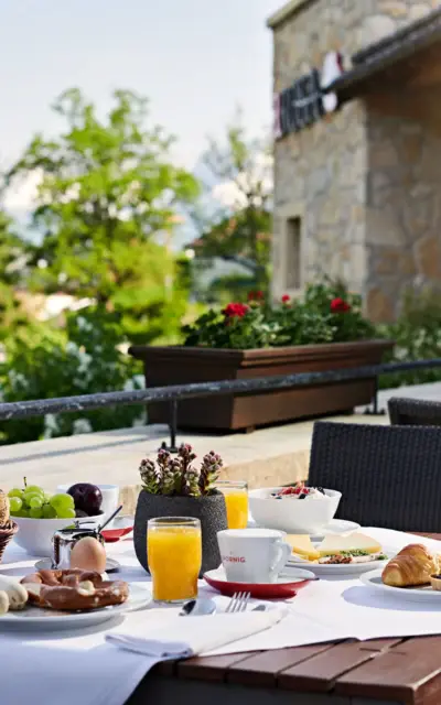 A breakfast table on a balcony with pastries, fruits and drinks overlooking the mountains. 