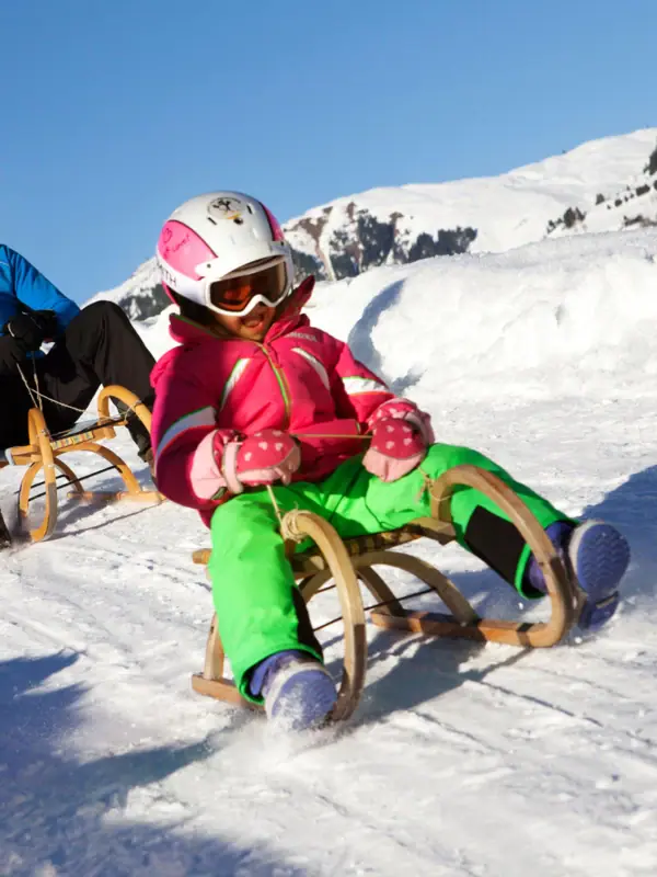 A man and a girl are sledging down a snow-covered slope.