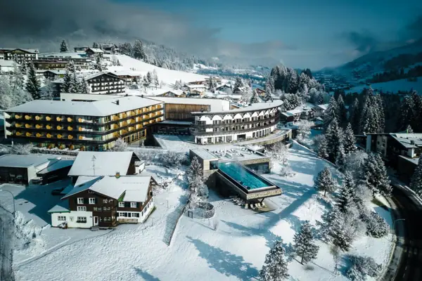 A snow-covered landscape featuring the A-ROSA Ifen Hotel Kleinwalsertal and trees.