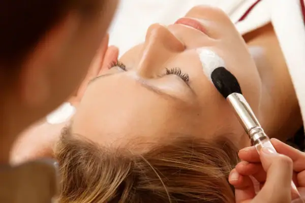 A woman receiving a facial treatment from a makeup artist.