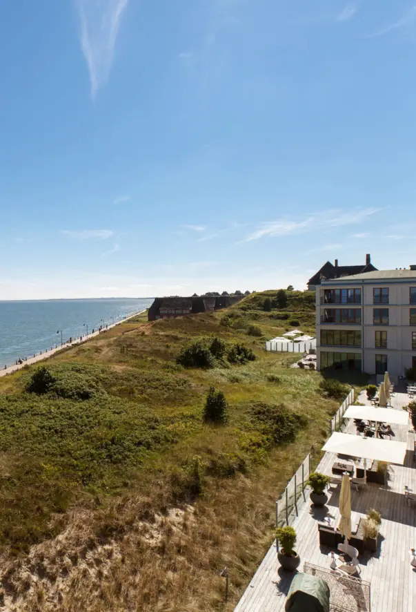 An aerial view of the green dunes and the blue waters of the Baltic Sea in bright sunshine.