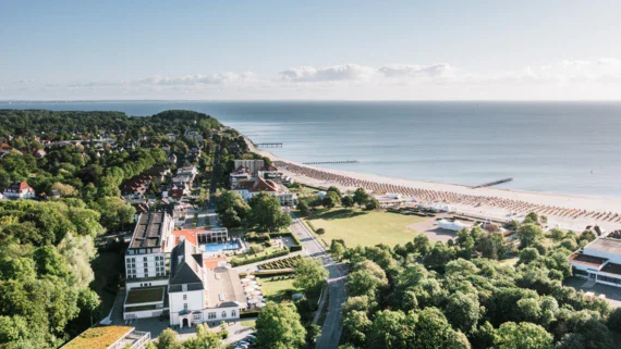 An aerial view of a coastal town with trees, houses, and a clear view of the shore and sea.