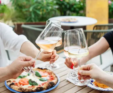 Group of people clinking glasses of wine over a wooden table with a pizza on it.