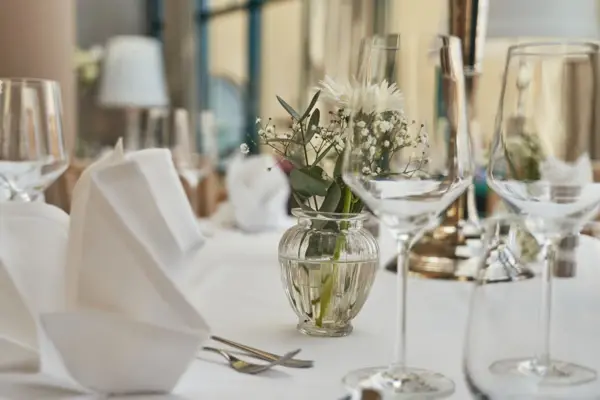 Elegantly set dining table with wine glasses, a vase of flowers, and tableware.