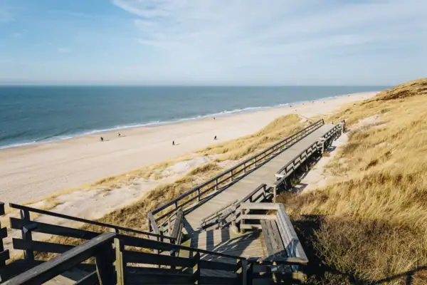 Holzsteg, der zu einem Strand führt, unter bewölktem Himmel.
