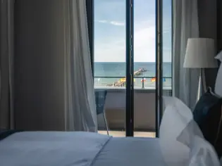 Interior view of a hotel room with a bed and sea view through the window.