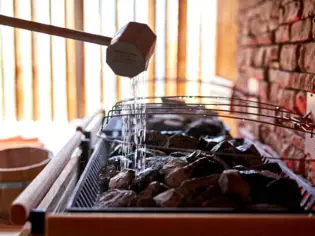 Water is poured from a ladle onto a sauna heater.