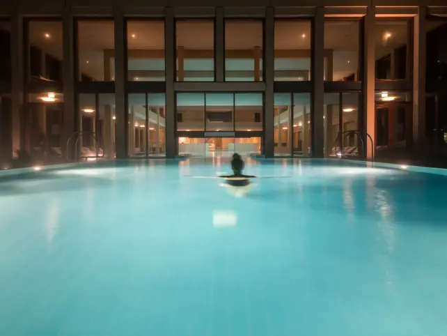 A woman swimming in an outdoor pool at night and a hotel SPA area in the background. 