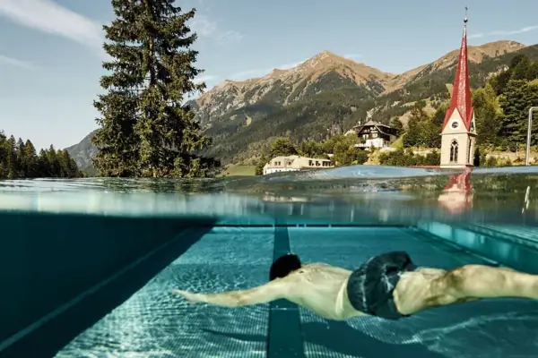 Man swimming in the infinity pool at Straubinger Grand Hotel with Alpine mountain view in Bad Gastein.