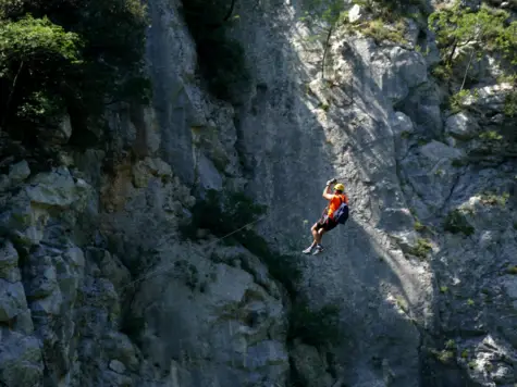 Person with a helmet hanging from a rope over a cliff.