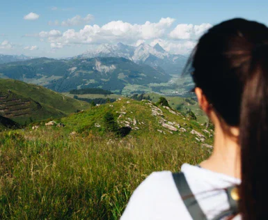 A woman photographed from the back is overlooking the green mountains around her. 