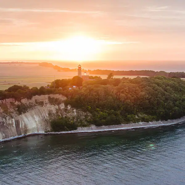 Lighthouse on a hill overlooking a body of water under a cloudy sky.