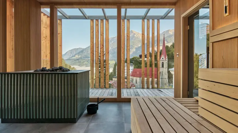 Sauna room with a view of mountains and a church through a large window.