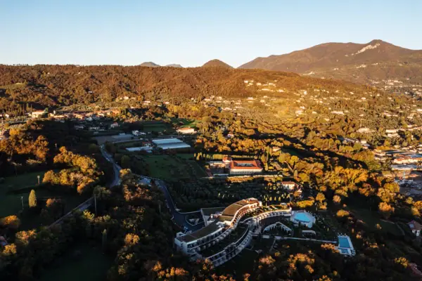 An aerial view of a landscape with trees and buildings, with mountains and the sky in the background.