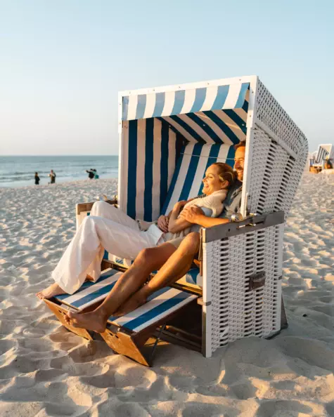 A couple happily sitting in a beach chair while the sun is setting. 