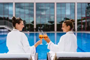 Zwei Frauen in weißen Bademänteln halten Getränke.