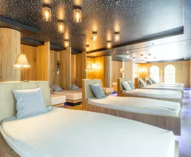 A relaxation room with multiple beds inside. Little lights on the ceiling and the beds fill the room with warm light. 