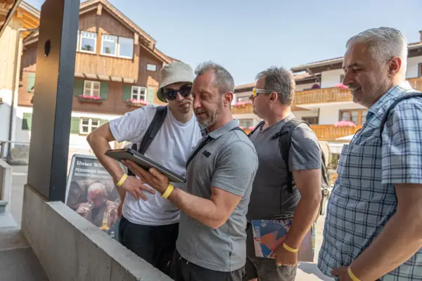 A group of men are standing outside looking at a tablet.