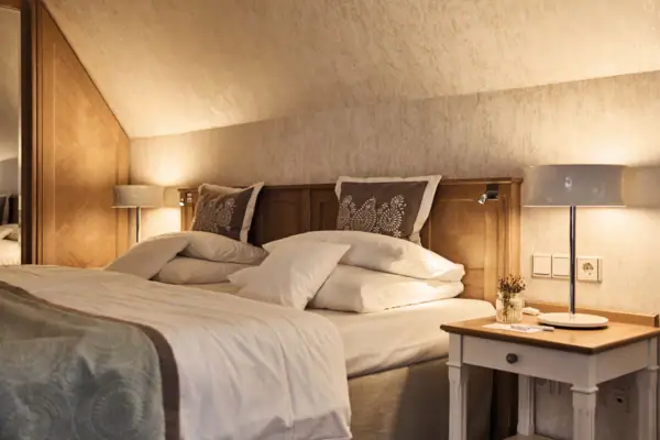 A neatly made bed with pillows and a nightstand featuring lamps.