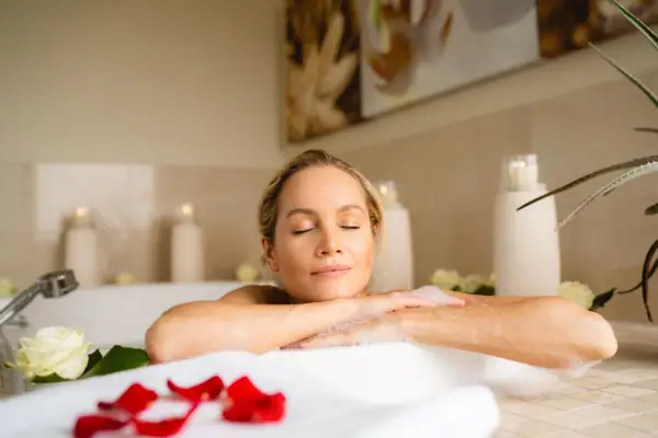 Einen Frau entspannt in einer Badewanne in einem Schaumbad und hat die Augen geschlossen.